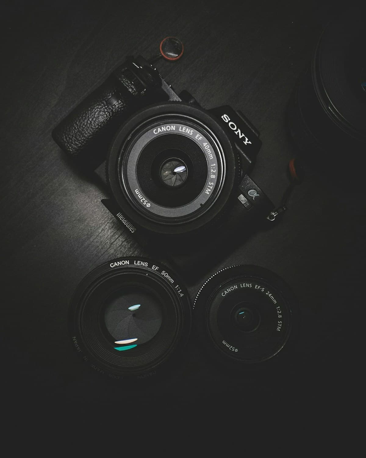 A black camera and separate lenses arranged on a dark surface.